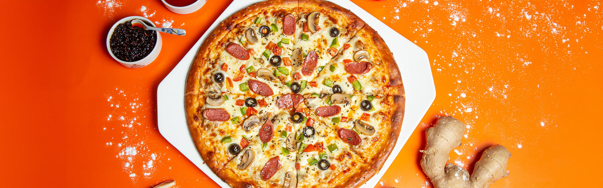 Eine Pizza mit Peperoni, Pilzen, Oliven und grünem Paprika liegt auf einem weißen Teller auf orangener Unterlage