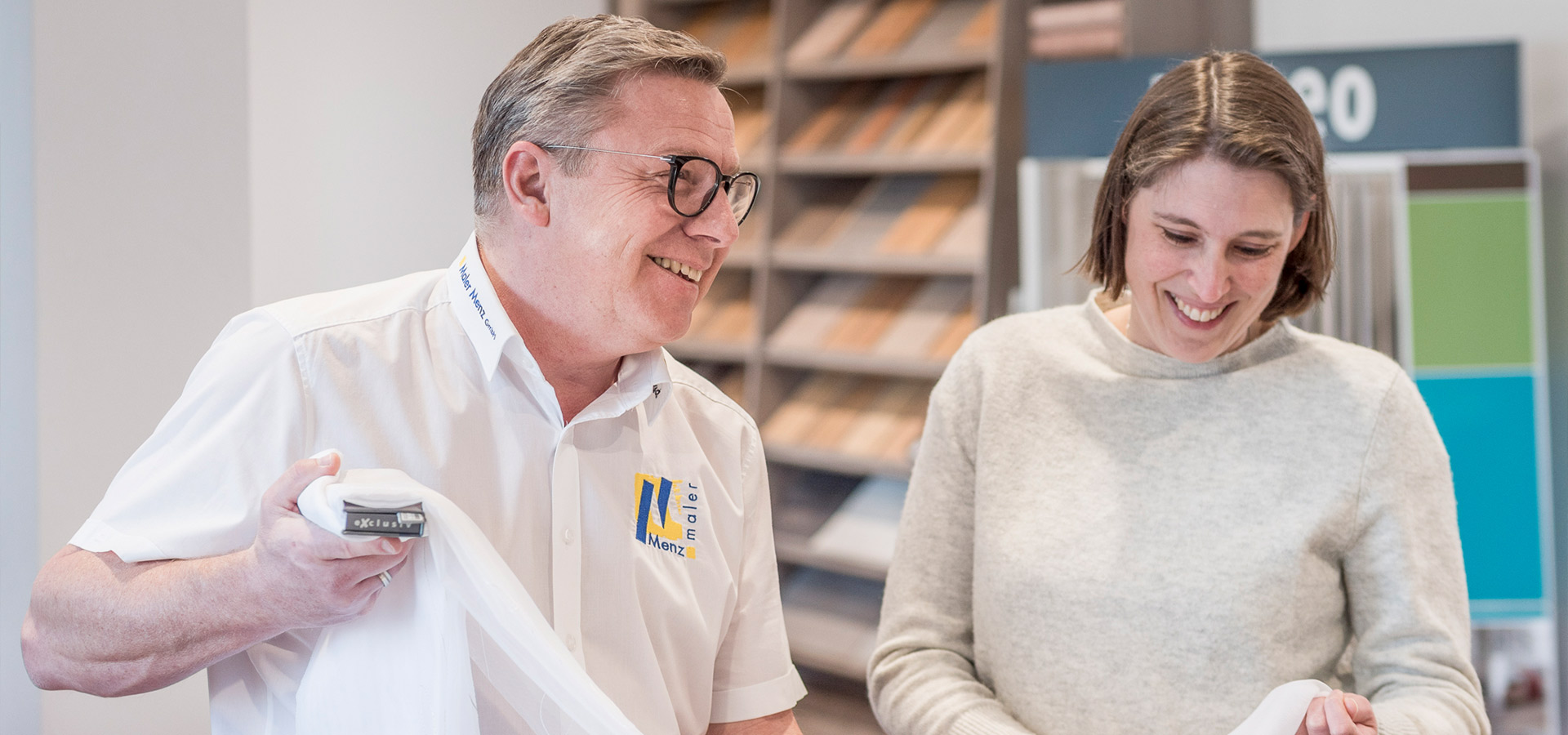 Zwei lächelnde Personen während einem Mitarbeitergespräch mit Farbproben im Hintergrund
