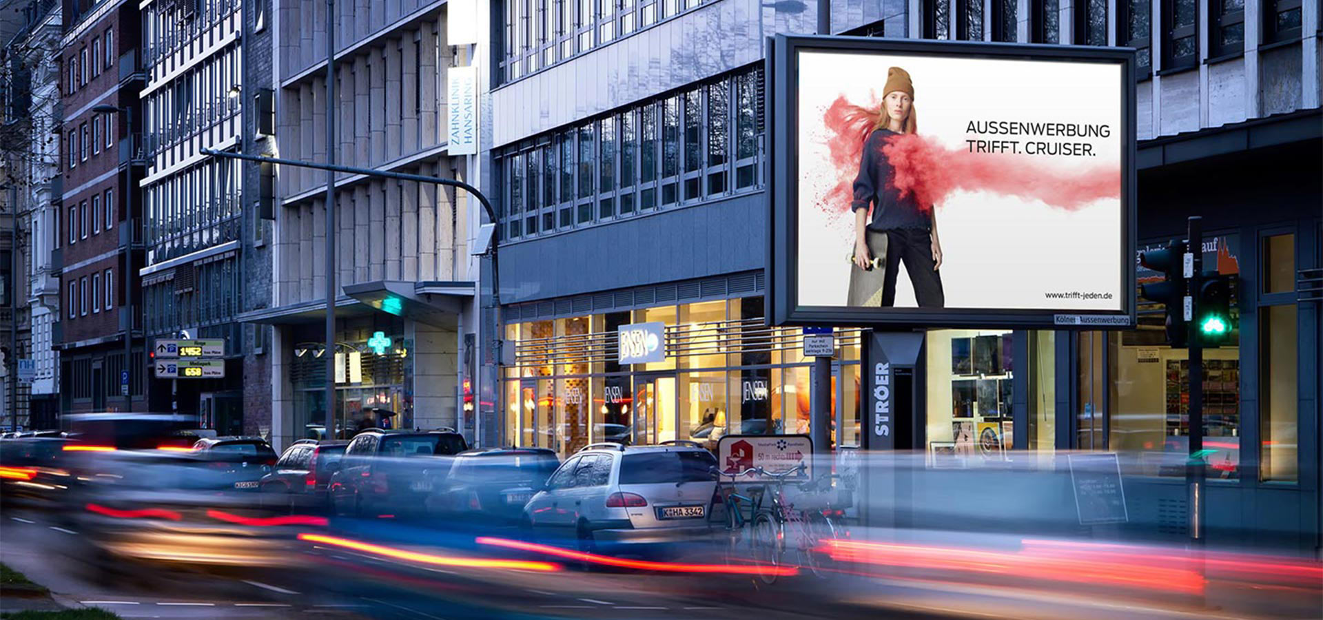 Plakatwand an einer belebten Stadtstraße zeigt eine Person in einem roten Outfit
