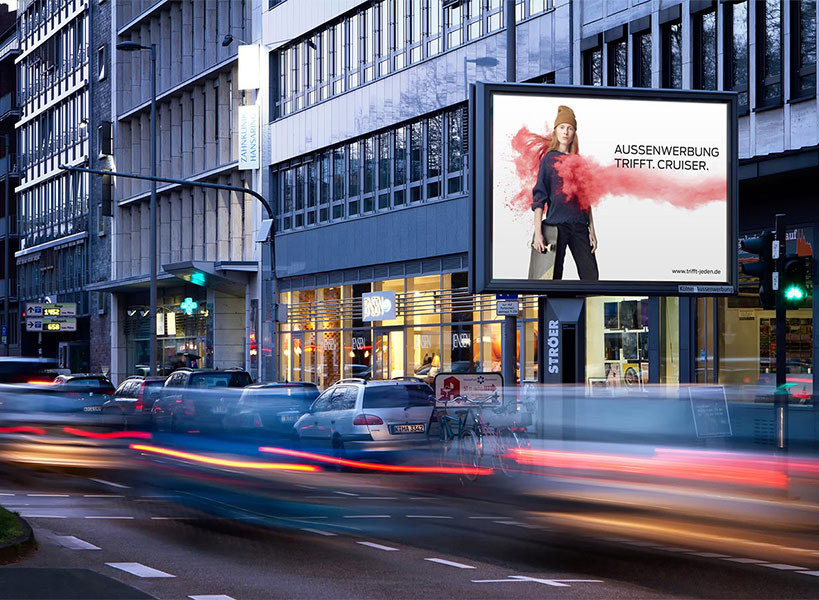 Plakatwand an einer belebten Stadtstraße zeigt eine Person in einem roten Outfit
