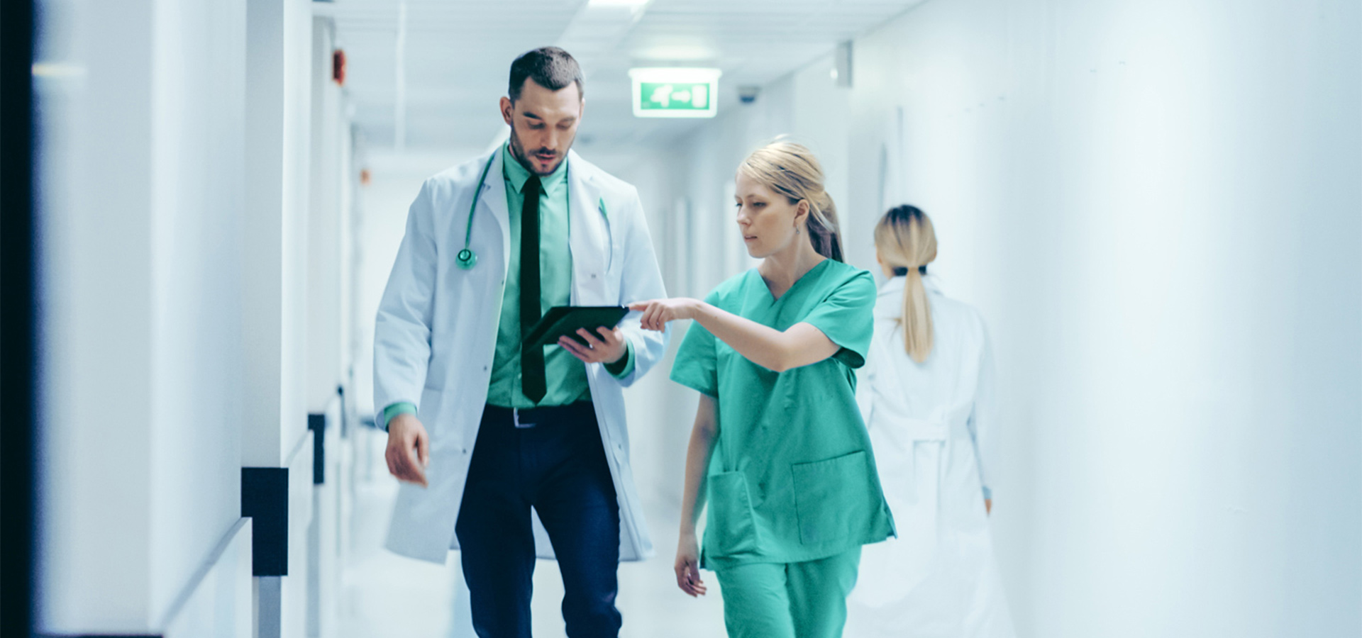 Arzt und Krankenschwester gehen einen Krankenhausflur entlang und schauen auf ein Tablet