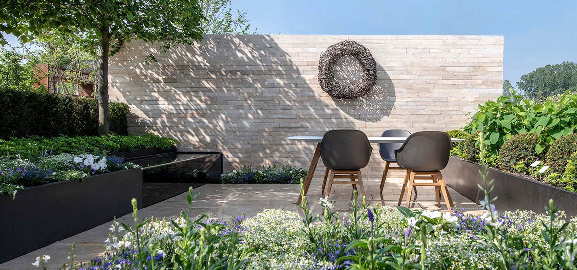 Moderner Außengarten mit Essecke, zwei schwarzen Stühlen und einem Tisch vor einer hellen Backsteinwand