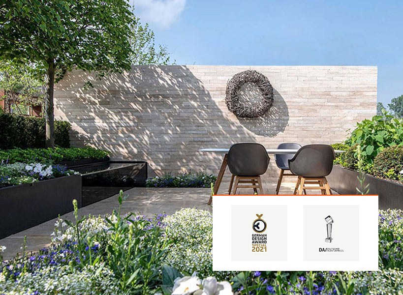 Moderner Außengarten mit Essecke, zwei schwarzen Stühlen und einem Tisch vor einer hellen Backsteinwand mit Awards