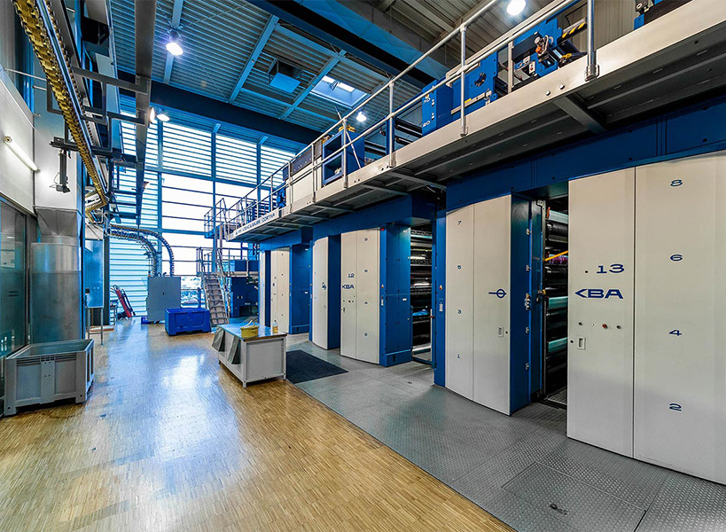 Große industrielle Druckmaschine mit blau-weißer Maschinerie, Bedienfeldern und Rohren