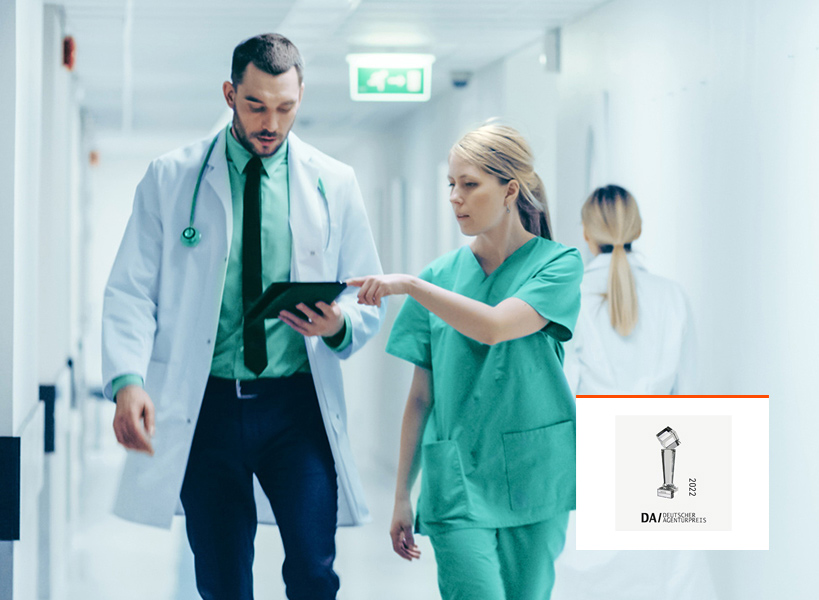 Arzt und Krankenschwester gehen einen Krankenhausflur entlang und schauen auf ein Tablet mit Award-Logo
