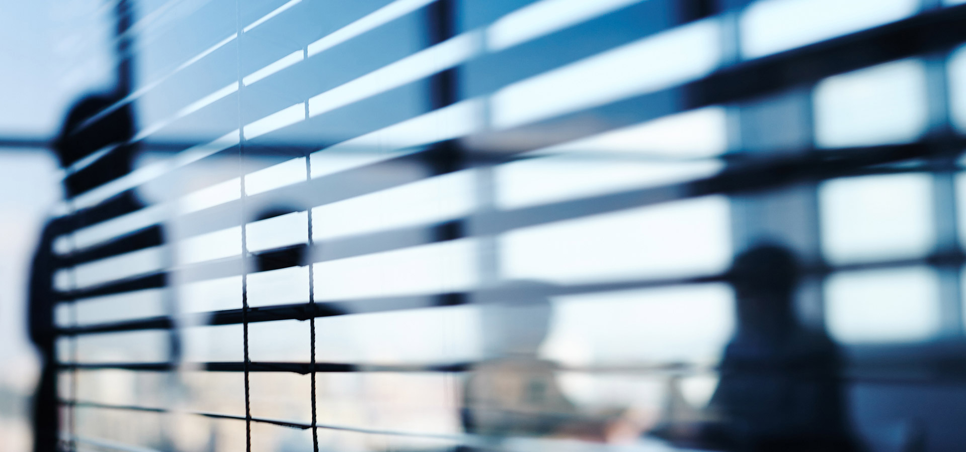 Blick durch horizontale Jalousien zeigt verschwommene Silhouetten von Menschen in einem Büro