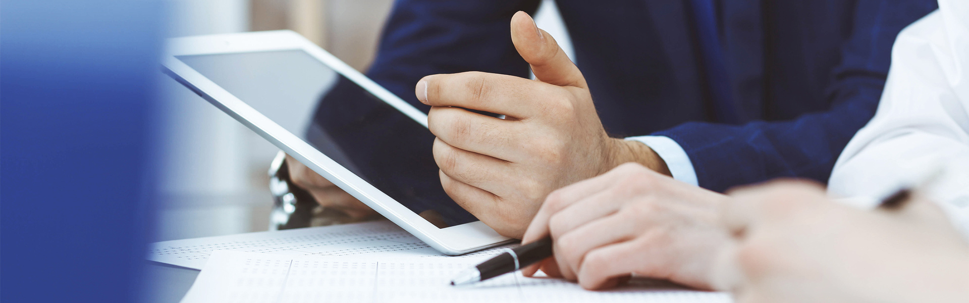Zwei Personen sitzen an einem Schreibtisch und überprüfen Informationen auf einem Tablet
