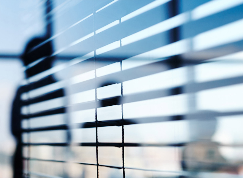 Blick durch horizontale Jalousien zeigt verschwommene Silhouetten von Menschen in einem Büro