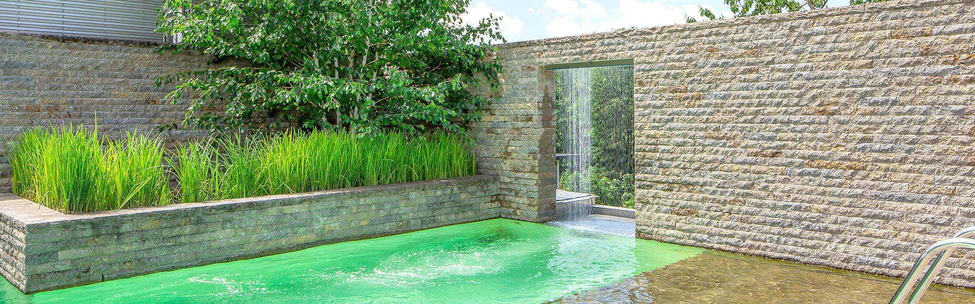 Moderner Swimmingpool mit türkisem Wasser umgeben von Steinmauer und Gräsern