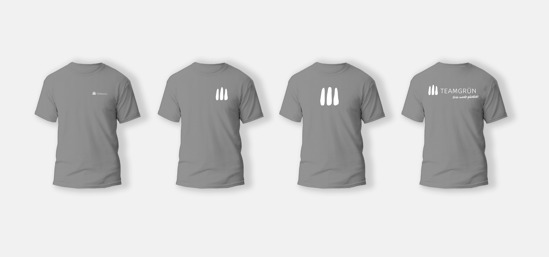Ansicht von vier grauen T-Shirts mit jeweils leicht unterschiedlichen Aufdrucken des Logos von Team Grün