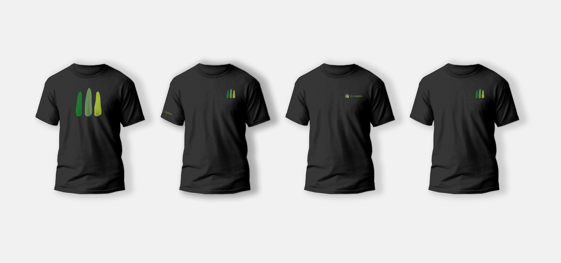 Ansicht von vier schwarzen T-Shirts mit jeweils leicht unterschiedlichen Aufdrucken des Logos von Team Grün