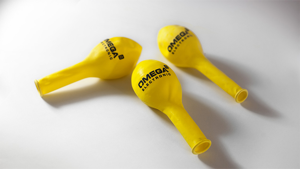 Ansicht dreier Luftballons im Corporate Design von Omega Electronics auf einem weißen Tisch