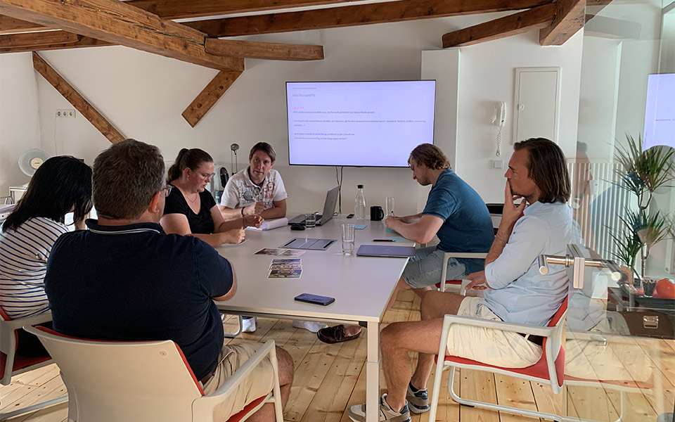 Abbildung einer Gruppe Menschen, die an einem Tisch sitzen und zusammen einen Workshop durchführen.