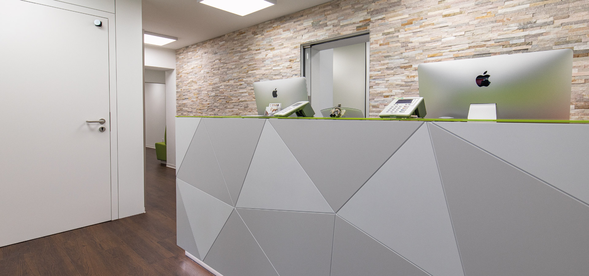 Empfangstheke in Praxisraum mit zwei iMac Computern vor Steinwand