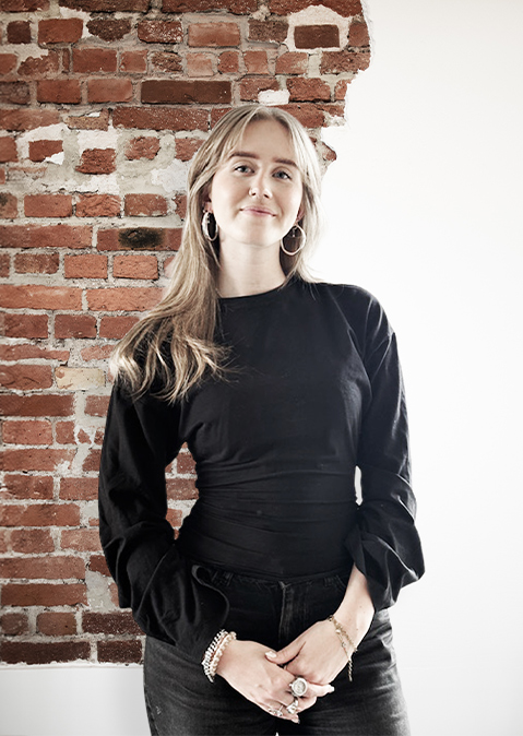 Frau mit schwarzem Oberteil steht vor einer gemauerten Wand