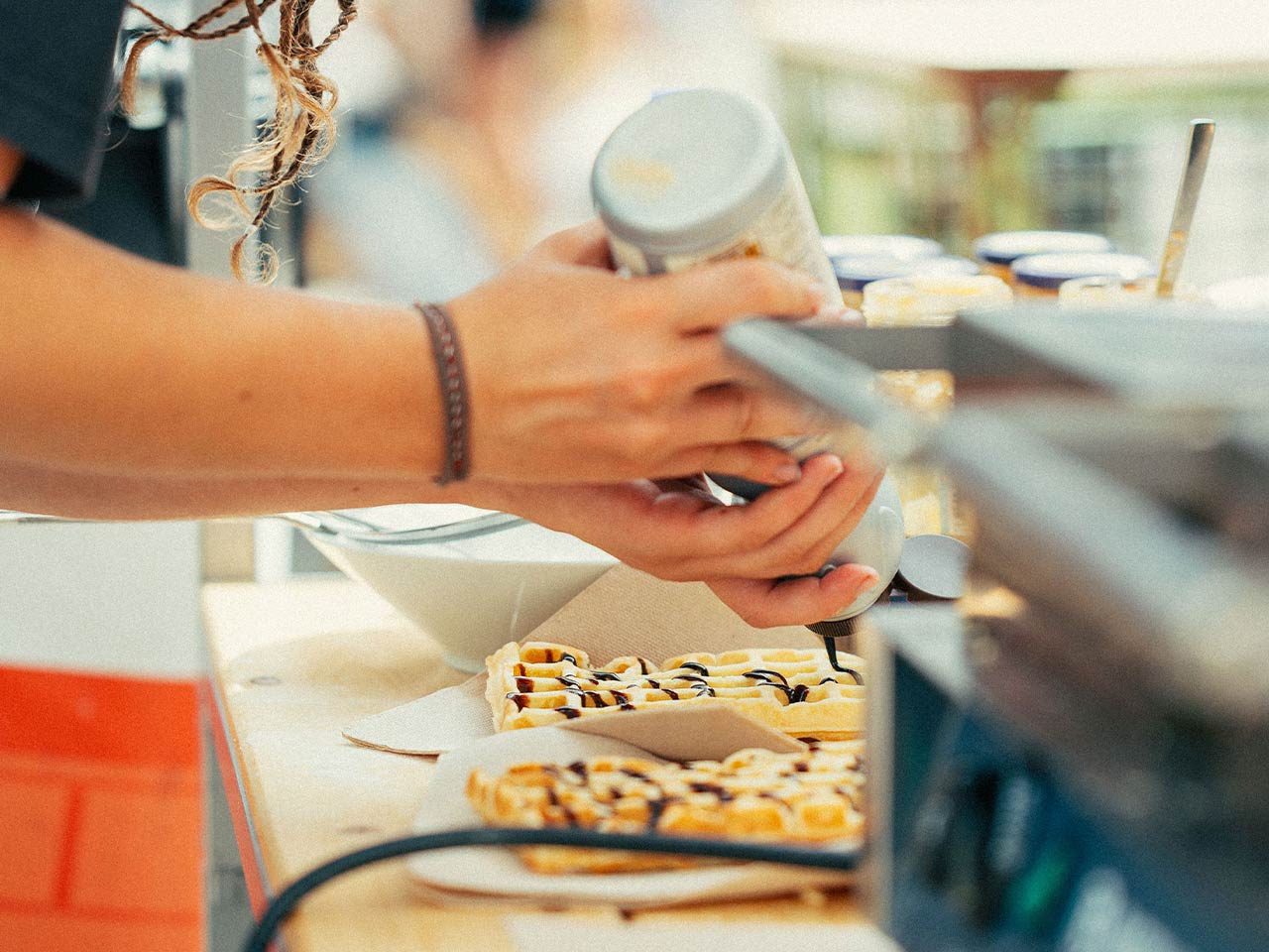 Abbildung zweier Frauenhände, die Schokoladensoße auf einer Waffel verteilen